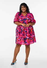 Vestido floral vibrante con tonos en rosa, rojo y azul marino. Mangas cortas abullonadas, escote en V y silueta en A. Tejido suave y fluido.
