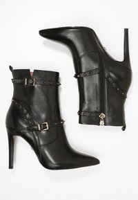 Bottines en cuir noir avec un bout pointu, un talon stiletto haut, des détails en métal doré et des accents cloutés. Dispose d'une fermeture éclair sur le côté.