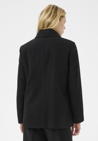 Abrigo de lana negro con cuello de muesca, corte recto, mangas largas y una textura suave con sutiles detalles de costura en la parte posterior.