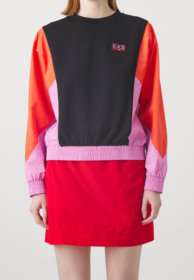 Sweat-shirt à blocs de couleurs avec manches noires, orange et roses, poignets élastiques ; associé à une jupe rouge. Tissu texturé avec détail logo.