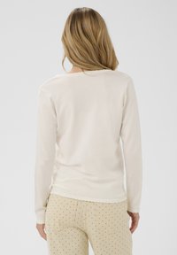 Long-sleeve cream top with a scalloped neckline, paired with beige pants featuring black polka dots, viewed from the back.