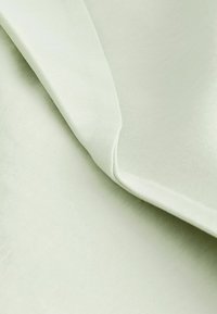 Tissu vert clair en gros plan montrant une texture lisse et des plis superposés avec des ombres douces.