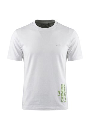 T-shirt Lacoste bianca a maniche corte con scollatura tonda, piccolo logo ricamato sul petto e scritta verde "LA CHEMISE LACOSTE PARIS" vicino all'orlo.