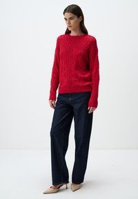 Maglione rosso lavorato a maglia con motivo testurizzato, dotato di maniche lunghe e scollo tondo. Abbinato a pantaloni a gamba larga in denim scuro e tacchi nude.