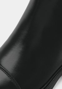 Μαύρο δερμάτινο μποτάκι αστραγάλου με λεία, γυαλιστερή υφή, με στρογγυλεμένη μύτη και διακριτική ραφή κατά μήκος των ραφών και του άνω μέρους.