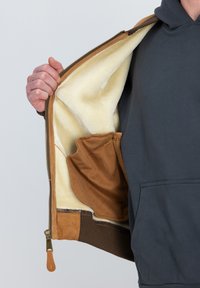 Chaqueta de ante marrón con forro de felpa crema; cuenta con un bolsillo lateral y puños de punto marrones; cierre dorado con tirador de cuero.