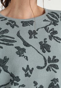 Hellblauer Pullover mit schwarzem Glitzer-Blumenmuster, runder Ausschnitt und weichem Strickmaterial, geeignet für Freizeitkleidung.