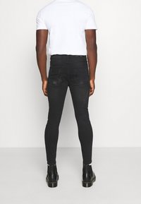 Černé skinny džíny s vysokým pasem, se hladkým povrchem a jemnými detaily zesvětlení. V kombinaci s černými kotníkovými botami.