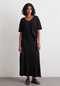 Schwarzes V-Ausschnitt-T-Shirt kombiniert mit einem passenden Maxikleid aus weichem Stoff. Das Model trägt schwarze Sandalen mit goldenen Schnallenakzenten.