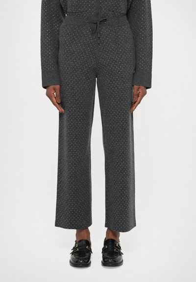 Pantaloni grigi a fantasia realizzati in tessuto morbido, caratterizzati da una vestibilità comoda, vita con coulisse e puntini bianchi sparsi. Indossati mocassini neri.