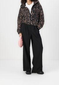 Chaqueta corta con estampado de leopardo en negro y marrón, combinada con pantalones de pierna ancha negros y un bolso de mano rosa. Textura suave, corte relajado.