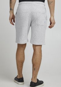 Shorts en coton gris avec une coupe décontractée, taille élastique et poche arrière avec logo. Texture lisse, design à longueur de genou.