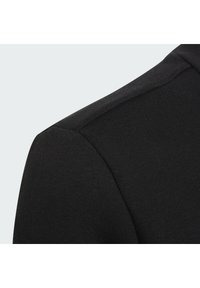 Primo piano di una spalla di una camicia di cotone nera che mette in evidenza la cucitura e la texture del tessuto su uno sfondo chiaro.