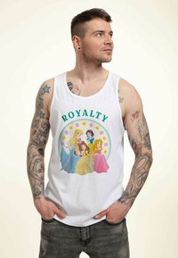 Camiseta sin mangas blanca con un gráfico colorido de princesas que presenta cinco personajes. Texto "REaleza" en verde sobre un diseño circular con flores y coronas.