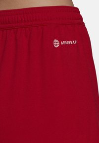 Rode sportieve shorts van gladde stof, met een elastische tailleband en een klein wit logo "AEROREADY" aan de zijkant.
