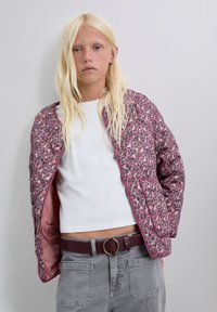 Chaqueta acolchada de leopardo en tonos rosa y gris con botones a presión, dos bolsillos frontales, llevada sobre una blusa blanca y combinada con pantalones grises.
