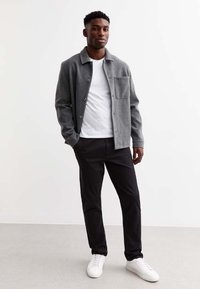 Chaqueta de mezcla de lana gris con cierre de botón y un bolsillo, usada sobre una camiseta blanca, combinada con pantalones negros y zapatillas blancas.