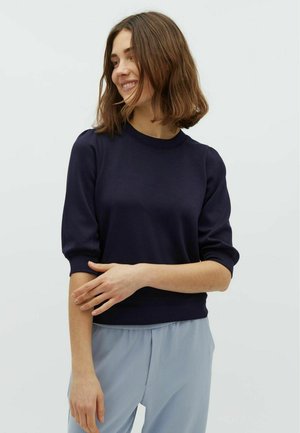 Dunkelblauer Pullover mit Rundhalsausschnitt und Puffärmeln, aus weichem Material gefertigt. Kombiniert mit hellblauen, locker sitzenden Hosen.