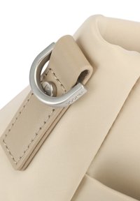 Borsa in tessuto beige con una texture liscia, dotata di un anello D in metallo argentato e un'etichetta in pelle cucita, che mostra dettagli di design minimalista.