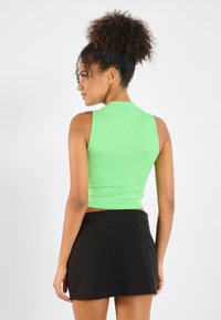 Top scurt verde cu dungi, cu un gât înalt, asociat cu o fustă mini neagră. Textură fină, design aderent și detalii minime.