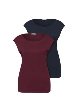 Dwie kobiety stoją obok siebie, jedna w beżowej kurtce i dżinsach trzyma brązową torebkę, druga w czarnym topie i jasnych dżinsach trzyma beżową torebkę.