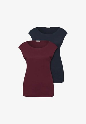 Deux femmes debout côte à côte, l'une portant une veste beige et un jean tenant un sac marron, l'autre un haut noir et un jean clair tenant un sac beige.