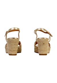 Sandalias de cuña en oro rosa con tacón de yute trenzado, tira en el tobillo y diseño entrelazado. Parte superior metálica suave y tacón texturizado.