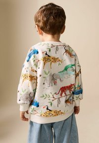 Hvid sweatshirt med mønstre af dyr og køretøjer i levende farver, afsluttet med ribstrikkede manchetter. Løs pasform, båret med lyse denimbukser.