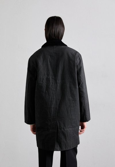 Cappotto lungo nero con superficie testurizzata, ampio colletto a scollo a V e vestibilità rilassata. Presenta una cucitura centrale sul retro e spalle scese.