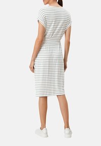Gestreiftes Midikleid in Weiß mit marineblauen Linien, kurzen umgeschlagenen Ärmeln, taillierter Passform und weichem Stoff, kombiniert mit weißen Sneakers.