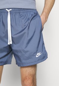 Nike simbyxor i ett mjukt blått tyg, med ett elastiskt midjeband och en vit dragsko, sidofickor och en vit logotyp vid fållen.