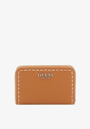 Portefeuille zippé en cuir tanné avec bordure blanche surpiquée et logo argenté "GUESS EST 1981" sur le devant.