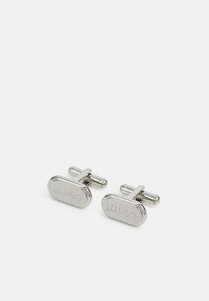 Abotoaduras prateadas em forma oval com um logotipo "HUGO" em relevo. Feitas de metal polido, têm um design minimalista e uma textura suave.