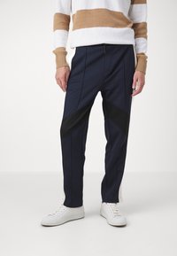 Navy sportbyxor med svarta diagonala paneler, med dragsko i midjan och avsmalnande ben. Stylar med vita sneakers.