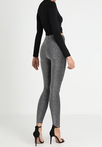 Hoog-wasit grijze leggings met een glinsterende textuur, gecombineerd met zwarte stiletto hakken en een aansluitend zwart langemouwen shirt.