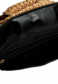 Wnętrze czarnej skórzanej torby o fakturowanym wykończeniu, z plecionym słomkowym obszyciem i kieszenią na zamek błyskawiczny. Widoczna miękka podszewka z tkaniny.