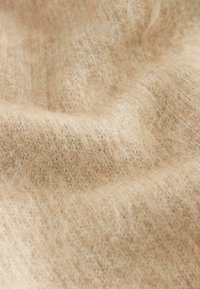 Tissu tricoté beige avec une surface douce et texturée, présentant de subtiles variations de couleur et une apparence chaleureuse et confortable.