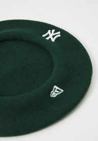 Zeleni filcani beret u okruglom obliku. Sadrži bijeli vezeni NY i logo naglaske. Mekana tekstura stvara glatku, strukturiranu formu.