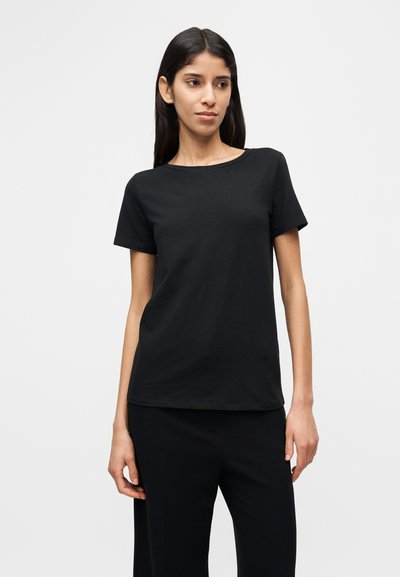 Μαύρο βαμβακερό μπλουζάκι με στρογγυλεμένο λαιμόκοψη και κοντά μανίκια, με άνετη γραμμή και λεία υφή, συνδυασμένο με μαύρο παντελόνι.