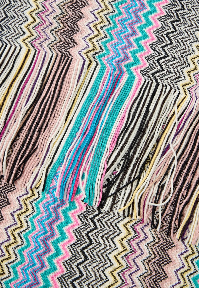 Multikleurige zigzag gebreide stof met lange franjes in roze, turquoise, zwart, wit, geel en beige tinten.