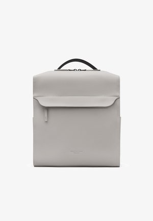 Mochila cuadrada minimalista de color gris claro con bolsillo delantero con cremallera, asa negra e impresión de logo sutil en el centro inferior.