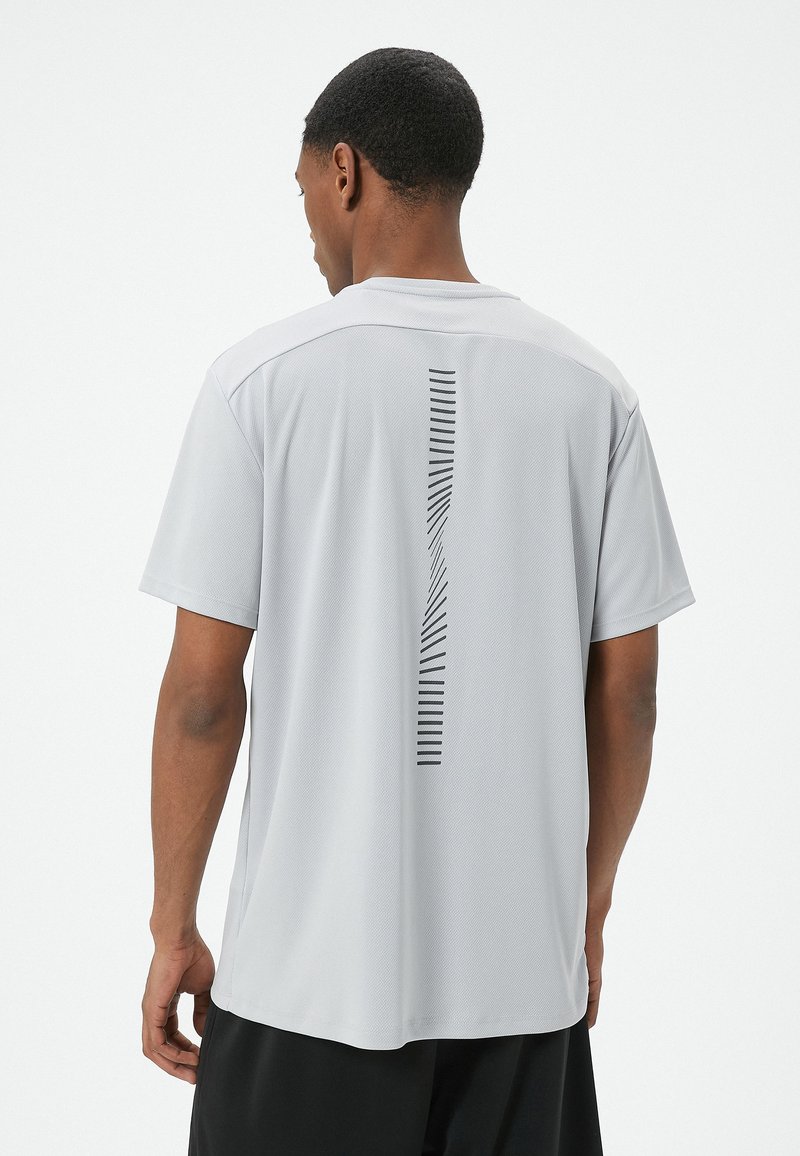 Camiseta atlética gris claro de manga corta, con un diseño de rayas verticales en la espalda y una textura transpirable.
