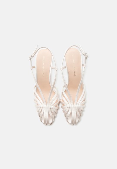 Λευκά σανδάλια με λουράκια και ανοιχτές μύτες, με κλεισίματα με αγκράφα, φαίνονται από πάνω σε απλό φόντο.