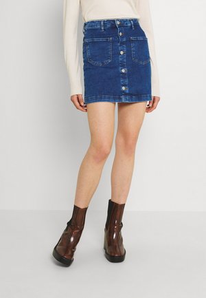 Denim mini krilo v modri barvi z sprednjim gumbom, dvema sprednjima žepoma in ravnim krojem. V kombinaciji s temno rjavimi gležnjarji.