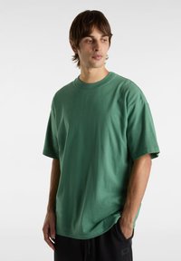 T-shirt vert oversize en coton, avec un col rond, des manches courtes et une texture lisse. Design simple sans motifs.