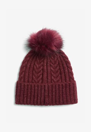 Burgundin värinen neulottu myssy, jossa on ribbikantti ja kohotettu siksak-kuvio. Huipulla on pörröinen pom-pom. Materiaali hohtaa hieman.