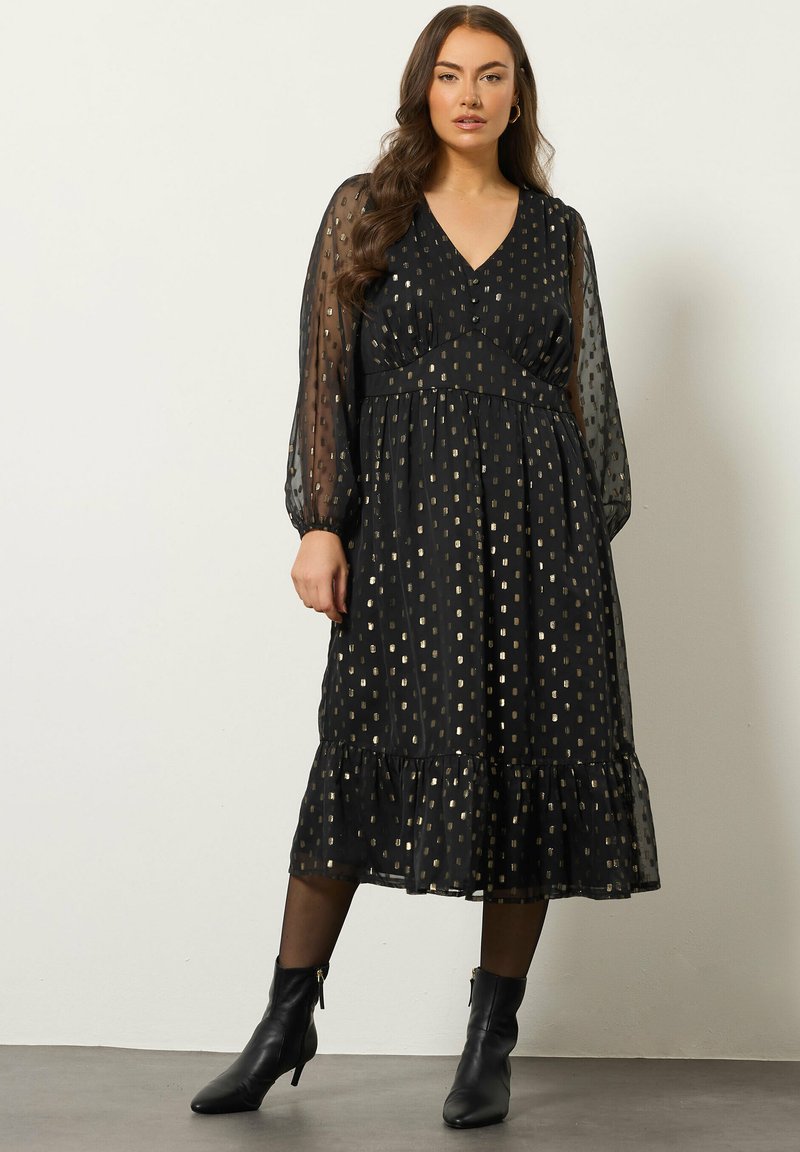 Mustan keskipitkän mekon, jossa on läpinäkyvät puffi-hihat, V-kaula-aukko ja kultaiset suorakulmio-kuviot. Leveä hameosa, jossa on kerroksellinen röyhelö.