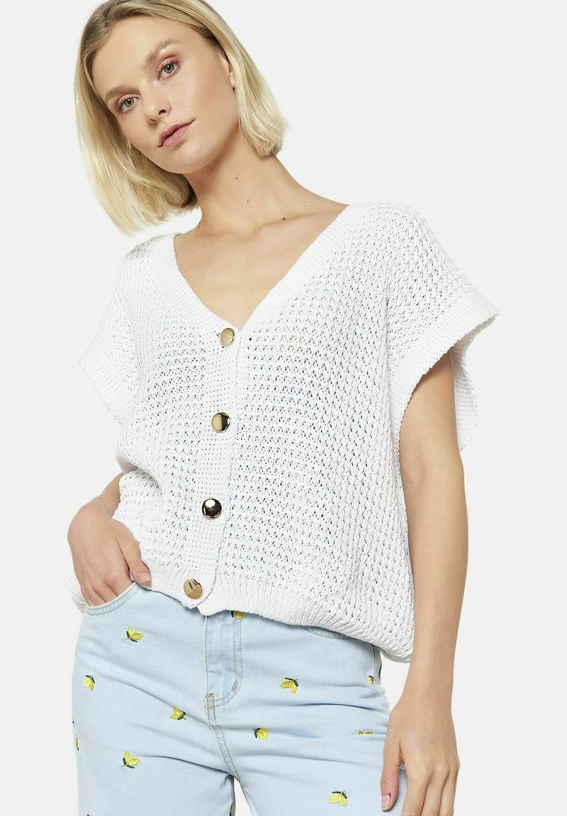 Top bianco a maglia con scollo a V e maniche corte, caratterizzato da grandi bottoni dorati lungo la parte anteriore. Tessuto testurizzato con un design a trama aperta.