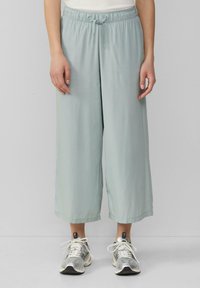 Hellblaue weite Hose aus glattem Material mit elastischem Bund und verstellbarem Kordelzug, kombiniert mit silbernen Sportschuhen.