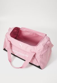Sac de sport rose en tissu durable. Il est doté d'un compartiment principal avec une fermeture éclair, de courtes poignées et d'une base noire.